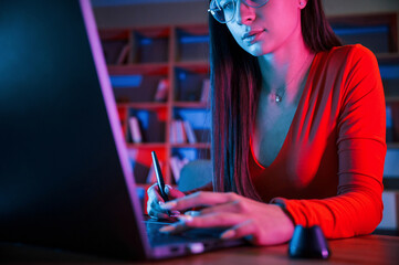 Young female retoucher working with computer and graphic tablet in neon lighting office