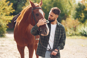 Front view. Young man with a horse is outdoors