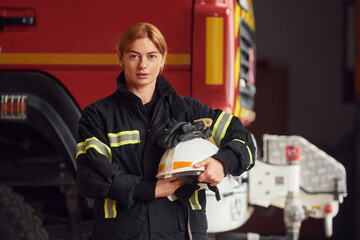 Fototapeta premium Holding helmet. Woman firefighter in uniform is at work in department