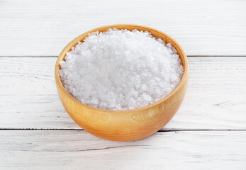 Sea salt in wooden bowl on white wooden background