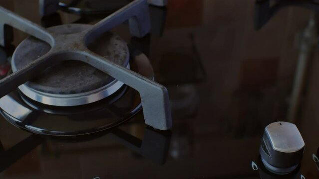 The hand turns off the gas on a modern gas stove. Blue flames of fire on black burners. The concept of using natural fuel in modern kitchens for cooking