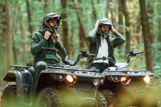Wearing helmets. Two male atv riders is in the forest together