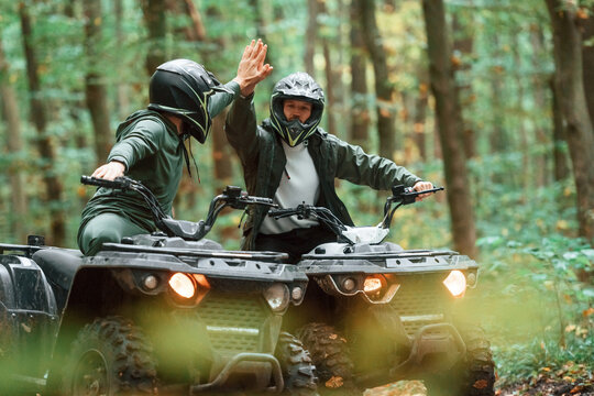 Giving high fives by the hands. Two male atv riders is in the forest together