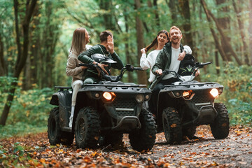 Smiling and having fun. Two couples on a quad bike in the forest during the day
