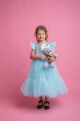 cute little girl in a beautiful dress holding a teddy bear on a pink background