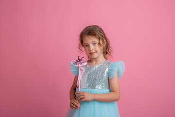 Obraz na płótnie Canvas cute little girl in a beautiful dress holding a fairy magic wand on a pink background
