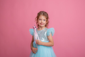 cute little girl in a beautiful dress holding a fairy magic wand on a pink background