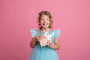 a cute little girl in a beautiful dress holds  a gift on a pink background