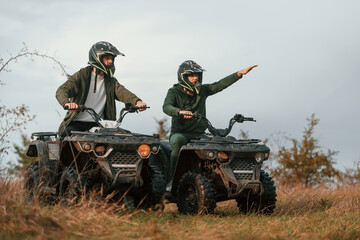 Showing the path by a hand. Two men are on the quad bikes outdoors on the field