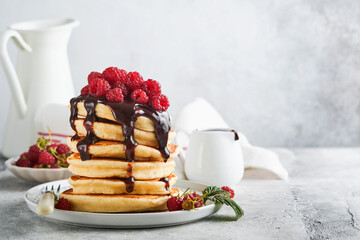 American pancakes. Stack pancakes with fresh raspberry with chocolate glaze or toppings in white bowl on light gray table background. Homemade classic american pancakes. Magazine concept. Top view.