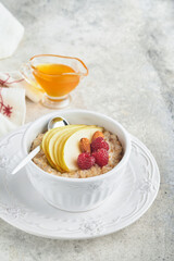Oatmeal. Bowl of oatmeal porridge with raspberry, pear and honey on gray concrete old table background. Hot and healthy food for Breakfast, top view, flat lay