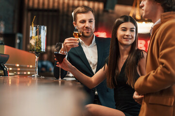 Woman and man sitting in the bar with drinks and welcoming their friend