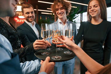Taking glasses with champagne. Group of people in beautiful elegant clothes are celebrating New Year indoors together