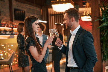 Man with woman is posing. Group of people in beautiful elegant clothes are celebrating New Year indoors together