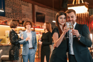 Man with woman is posing. Group of people in beautiful elegant clothes are celebrating New Year indoors together