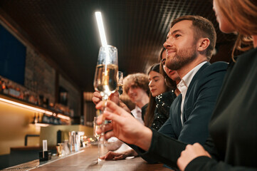 Sitting by the bar table. Group of people in beautiful elegant clothes are celebrating New Year indoors together