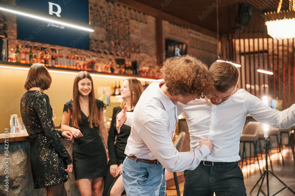 Wall mural Two men are having fun. Group of people in beautiful elegant clothes are celebrating New Year indoors together