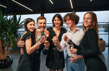 Sparklers light. Group of people in beautiful elegant clothes are celebrating New Year indoors together