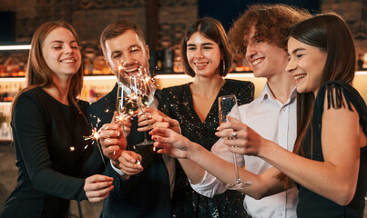 Amazing sparklers. Group of people in beautiful elegant clothes are celebrating New Year indoors together
