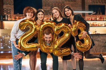 2023 is coming. With balloons. Group of people in beautiful elegant clothes are celebrating New Year indoors together