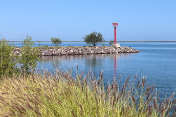 Small red lighthouse at the end of a breakwater and the entrance to a port in a bay of La Paz in...