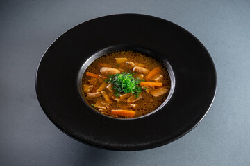 black plate with brown soup pottage with mushroom, carrot, vegetables, dill