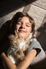 portrait of a female child with a dog fluffy jack russell on the floor with closed eyes and  smile