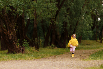  Happy funny baby under autumn shower. Girl running merrily laughing in the rain