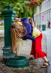 Beautiful blonde girl drinks from a public fountain