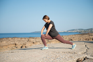 Fototapeta na wymiar Woman in sportswear doing stretching exercise at seaside. Female practicing workout outdoors during sunny day