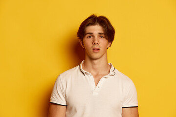 Portrait of young man in casual white T-shirt posing with shocked expression over yellow background