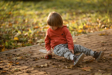 Naklejka na ściany i meble a little boy rides a skateboard in the park in the fall