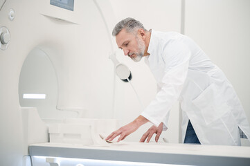 Male gray-haired doctor in a lab coat preparing MRI scanner