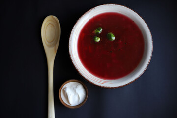 national Ukrainian dish red borscht from vegetables with meat in a plate with greens and next to a dark background a wooden spoon and sour cream in a bowl. for banners labels screensavers books with r