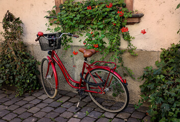 Ein knallrotes Damen Fahrrad mit Korb an einer Hauswand.