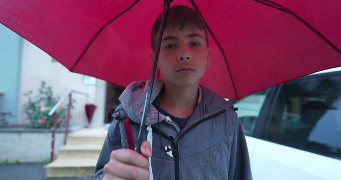 Adolescent kid walking outside in the rain holding umbrella. Raining afternoon in city. Young boy walks in rainy day