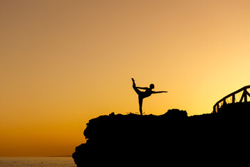 Woman doing yoga under a beautiful sunset in the coast. Flexible person silhouette doing exercise...