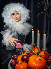A beautiful girl in a vintage black dress, a white frill and a lush curly wig is sitting at a table...