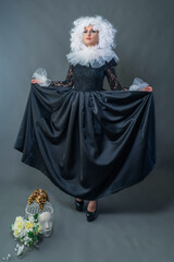 A beautiful girl in a vintage black dress, a white frill and a lush curly wig poses in the studio....