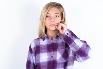 beautiful caucasian teen girl wearing plaid purple shirt over white wall mouth and lips shut as zip with fingers. Secret and silent, taboo talking.