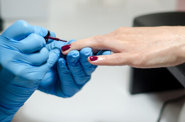 Female manicurist in blue gloves works with young hands and nails under a bright lamp. Process of applying gel polish on nails