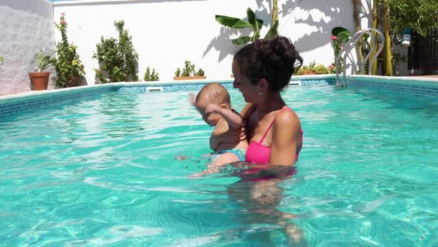horizontal video of a mom playing with her baby in the pool for the first time, 4k, slow motion