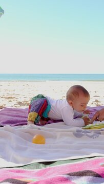 baby on a towel on the beach playing with balls and being surprised to discover sounds of toys, 4k, slow motion