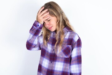 A very upset and lonely beautiful caucasian teen girl wearing plaid purple shirt over white wall crying,