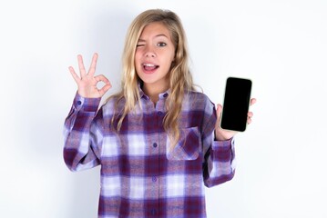 beautiful caucasian teen girl wearing plaid purple shirt over white wall holding in hands cell...