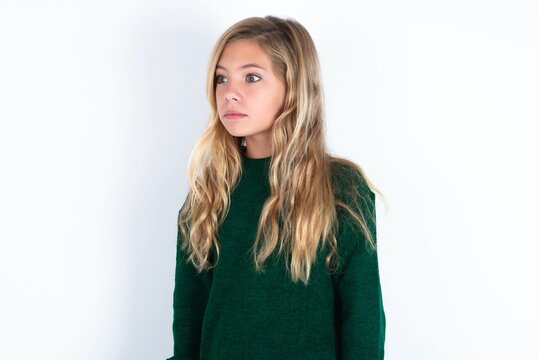 Beautiful Caucasian Teen Girl Wearing Green Knitted Sweater Over White Wall Stares Aside With Wondered Expression Has Speechless Expression. Embarrassed Model Looks In Surprise