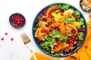 Poster Fresh autumn pumpkin salad with baked pumpkin slices, red cabbage, avocado, arugula, pomegranate seeds and walnuts. Healthy vegan, vegetarian eating, comfort food. White background. Top view © 5ph