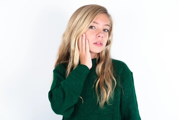 Photo of beautiful caucasian teen girl wearing green knitted sweater over white wall enjoy fresh perfect smooth skin touch face
