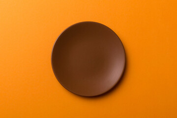 Top view of isolated of colored background empty round brown plate for food. Empty dish with space...