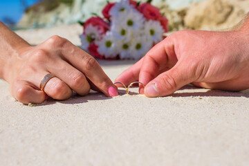 Couple holding wedding rings on beach. Gold marriage rings on the light sand background with copy space web banner template. Wedding concept, honeymoon